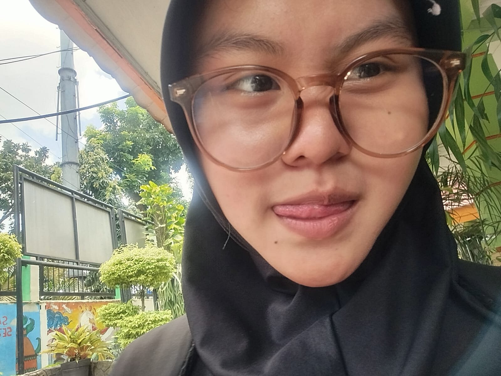Close-up selfie of Nadhira wearing glasses and a black hijab
